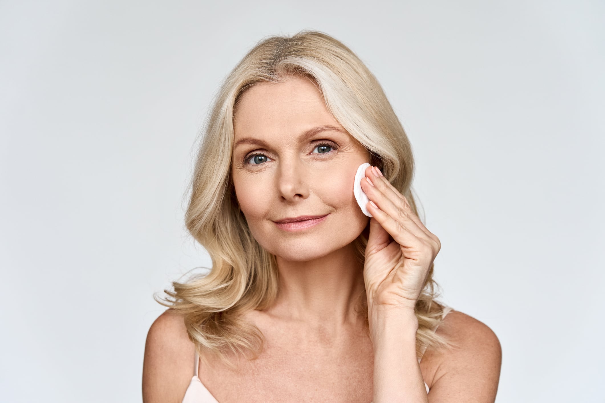 Portrait isolated on white of beautiful middle age 50 woman doing her everyday routine removing her makeup with cotton pad enjoying anti age healthy perfect products skin. Beauty and care advertising.