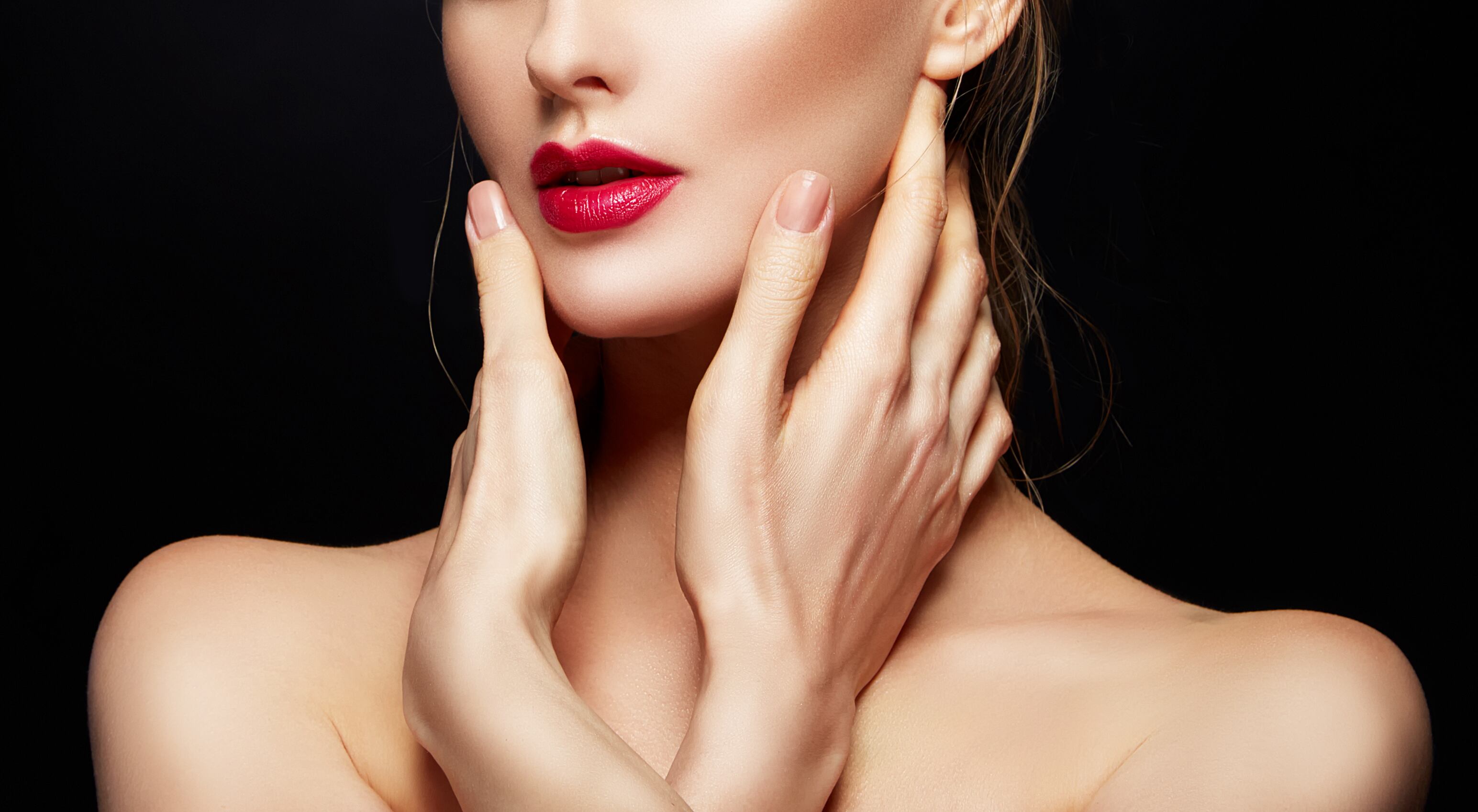 Part of model woman face with lips, hands and shoulders with bright red lips make-up and clean skin over black background