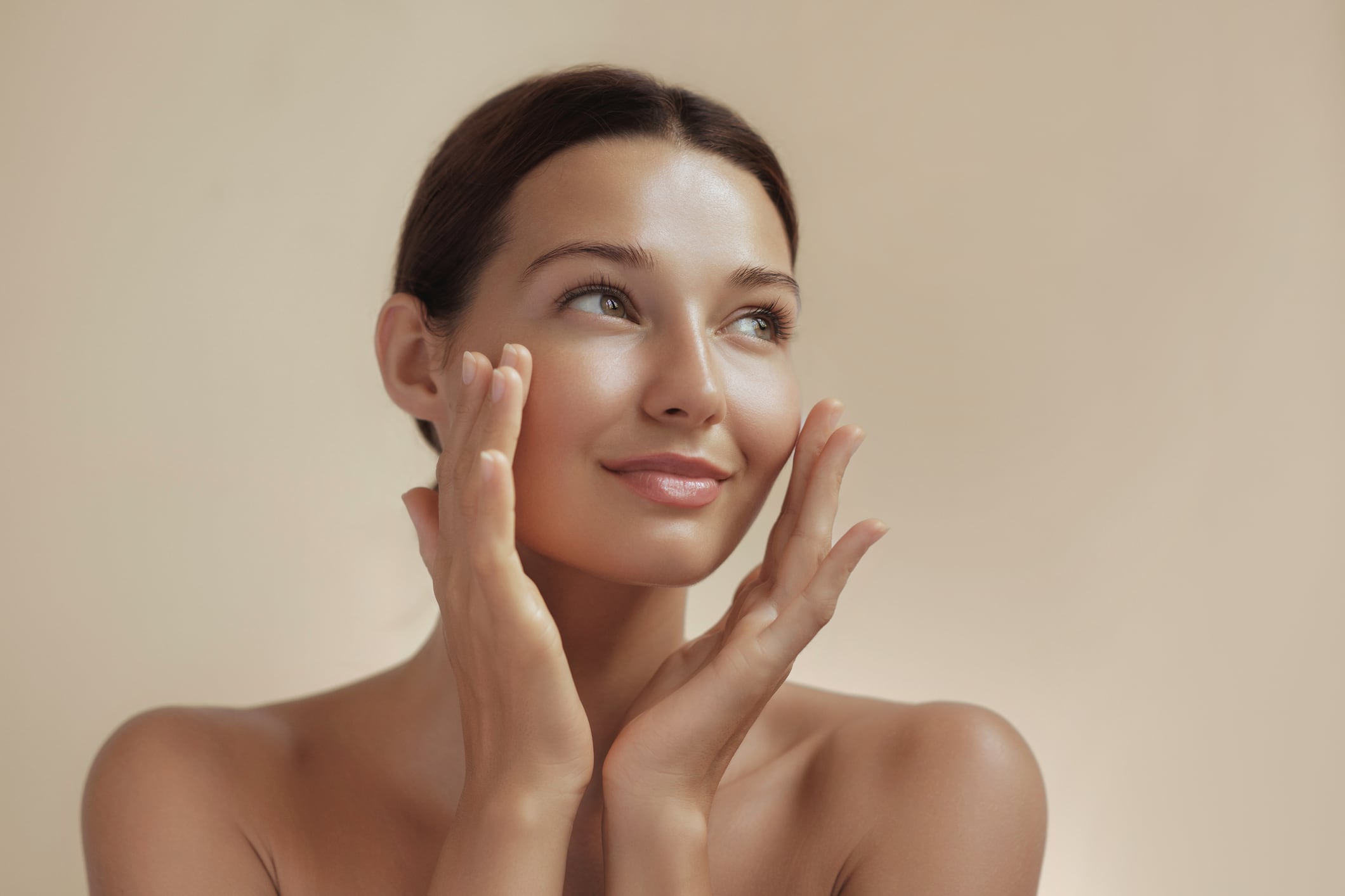 Skincare and Beauty Portrait. Woman with beautiful face touching healthy facial skin. Young adult smiling girl model with natural makeup on pink background closeup. High-quality beauty product or treatment conceptual photo