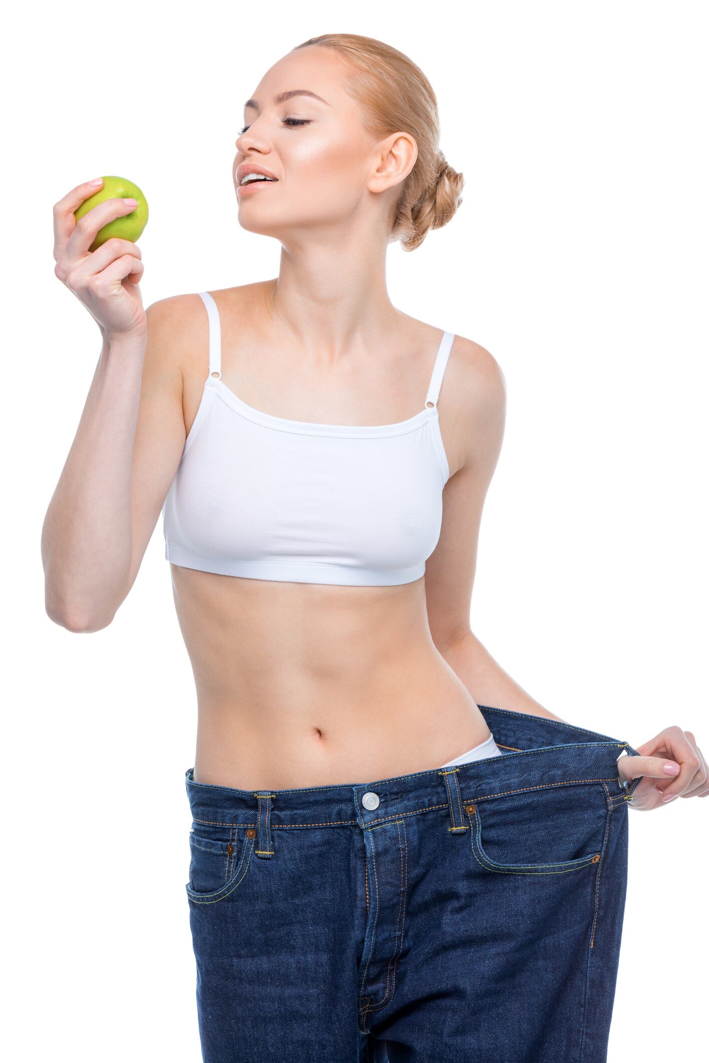 GLP-1 drugs: Ozempic; Wegovy Young smiling slim woman in oversized jeans holding apple on white
