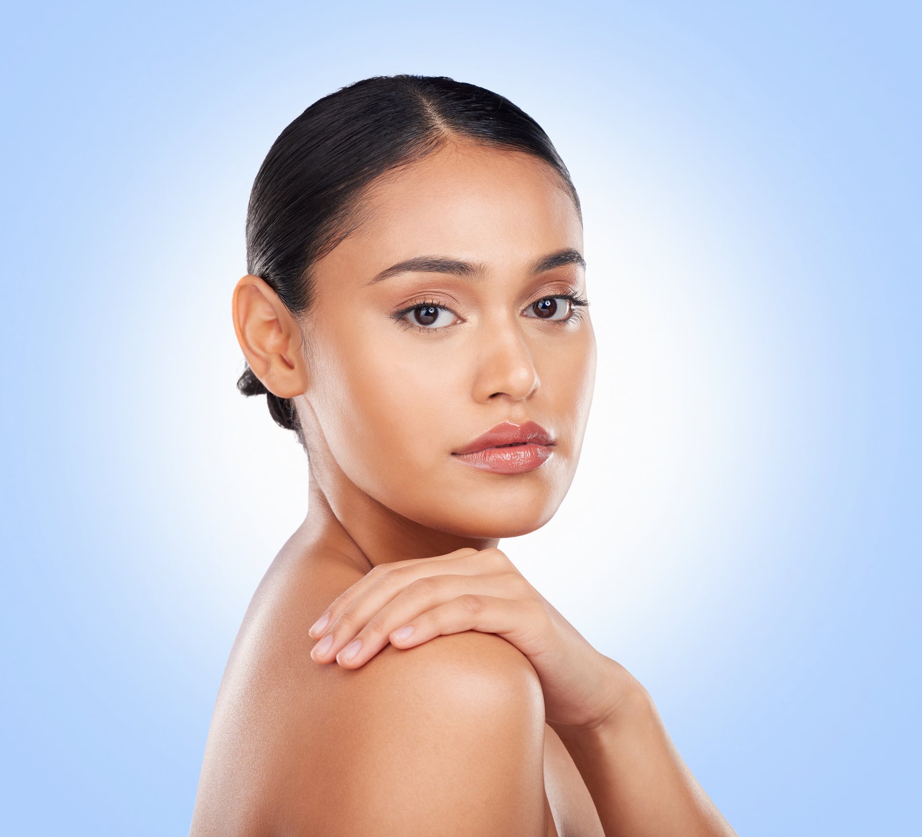 Portrait, glow and a woman with skincare on a blue background for wellness, beauty and health. Moisture, spa and a girl or model touching skin for cosmetics, dermatology or grooming on a backdrop